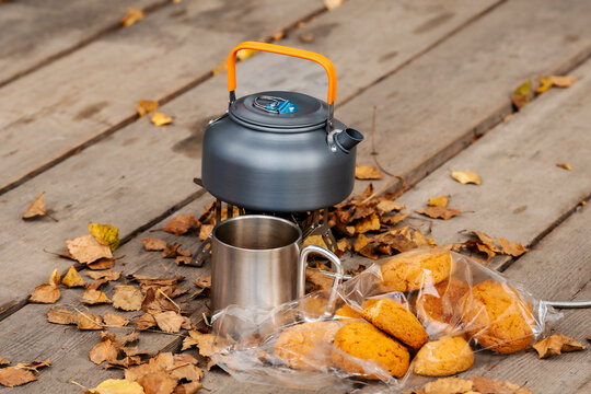 Kettle on a gas burner, glass and cookies on a wooden deck. Autumn atmosphere in the fresh air.