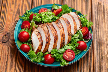 Grilled chicken breast ( fillet ) with lattuce salad and cherry tomatoes . Top view
