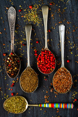 Old spoons with various seeds and spices on black background. Flat lay. Top view. Food concept. Dark mood food photography.