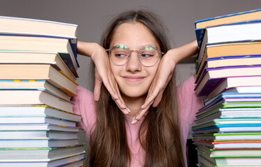 Thoughtful student surrounded by tall stacks of books. A young student with glasses sits at a desk...
