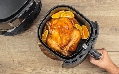 hand cooking delicious roasted whole chicken with oranges in air fryer on a wooden table. top view