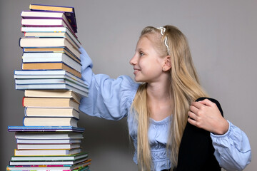 Young girl sitting with a tall stack of colorful books. A young girl with long blonde hair sits smiling next to a tall stack of colorful books.