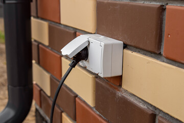 Outdoor electrical outlet on the wall of brick house. A wire with plug in the outlet. Double...