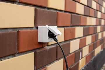 Outdoor outlet on the wall of brick house. A wire with plug in the outlet