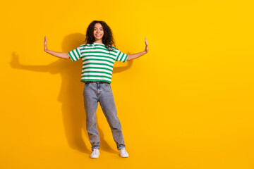 Full size photo of pretty young girl arms push empty space wear striped t-shirt isolated on yellow color background