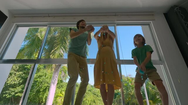 A pregnant woman, her husband, and their elder son conduct a gender reveal party. Throw blue confetti into the air in their excitement after they discovered that they are going to have a boy