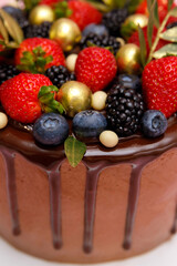 A beautifully decorated chocolate cake features an assortment of vibrant strawberries, blueberries, blackberries, and golden embellishments