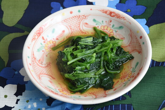 Horenso ohitashi is a Japanese dish of blanched spinach soaked in a light dashi broth. It's served chilled with soy sauce and topped with bonito flakes, offering a refreshing and savory flavor.