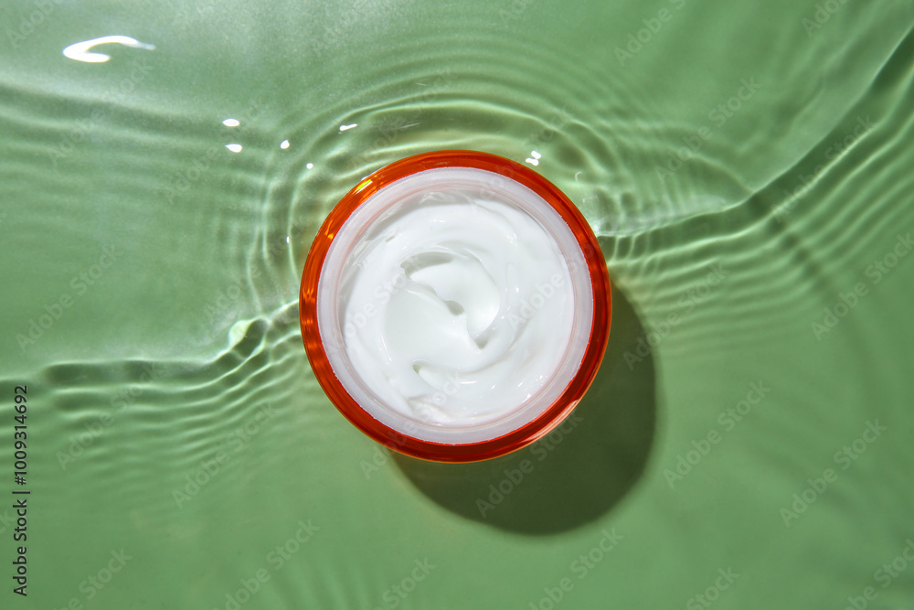 Poster Jar with cream in water on light green background, top view. Cosmetic product