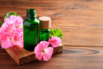 Geranium essential oil in bottles and beautiful flowers on wooden table, space for text
