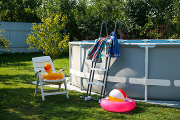 Above ground swimming pool, folding chair, towel, inflatable rings and ball in backyard