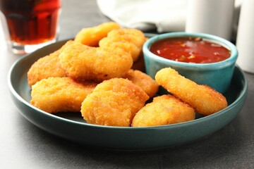 Plate with hot chili sauce and nuggets on grey textured table, closeup