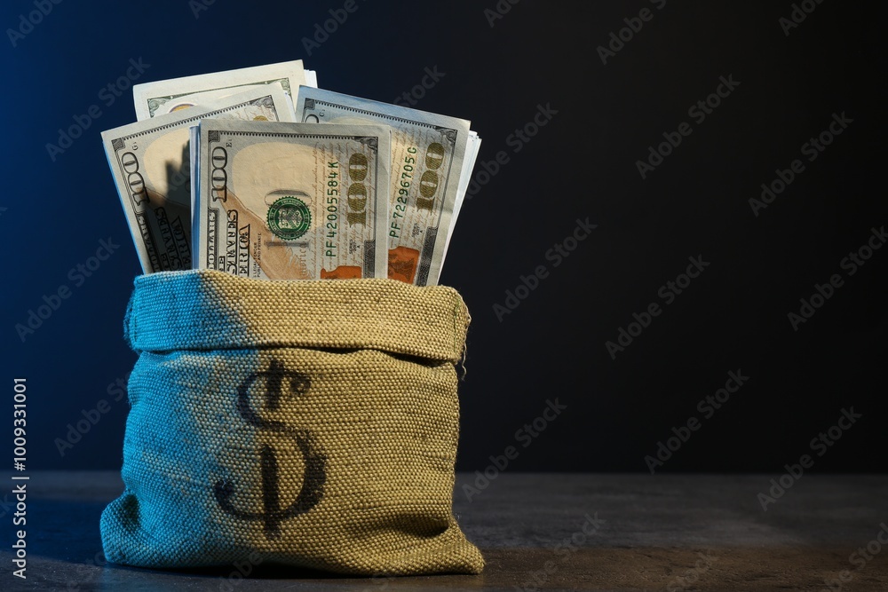 Wall mural Dollar banknotes in burlap sack on grey table against dark background in neon lights, space for text