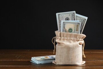 Dollar banknotes in burlap sack on wooden table against dark background