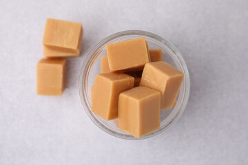Tasty sweet caramel candies in glass jar on light table, top view