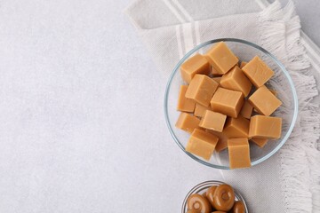 Tasty sweet caramel candies in bowls on light grey table, flat lay. Space for text