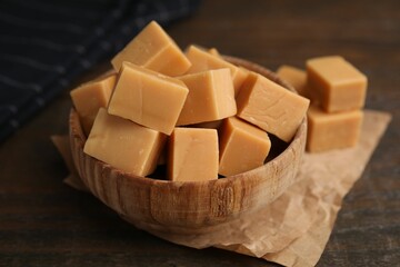 Tasty sweet caramel candies in bowl on wooden table, closeup