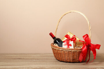 Wicker gift basket with wine on wooden table, space for text
