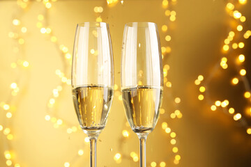Glasses of sparkling wine against golden background with blurred lights, closeup. Christmas decor
