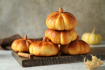 Tasty pumpkin shaped buns and cinnamon on light grey table, closeup