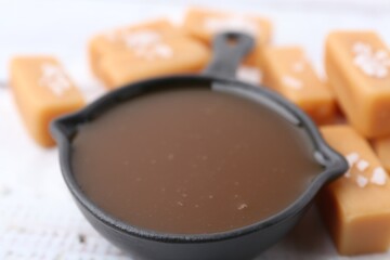 Tasty salted caramel in gravy boat and candies on table, closeup