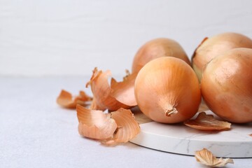 Fresh onions with peels on light table, closeup. Space for text