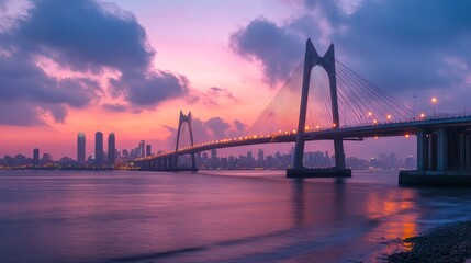 Fototapeta premium A bridge with lights on it during sunset with buildings in the background.