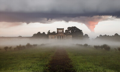 A majestic 19th-century villa sits amid autumn fog, with a historic garden and a long driveway leading toward it.