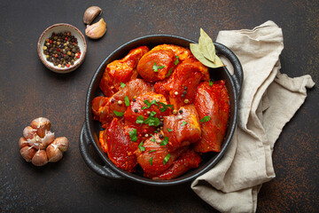 Raw uncooked chopped pieces of meat marinated with seasonings and parsley in black casserole dish top view on dark rustic background. Cooking ragout stew with marinated meat fillet pieces.