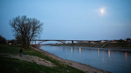 Obraz premium A tranquil reflection of a treeas shadow on water, illuminated by the full moon, with the silhouette of a man fishing softly outlined, no people.