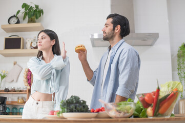 Young woman raised her hand to stop young man, refusing to eat a hamburger in her husband's hand