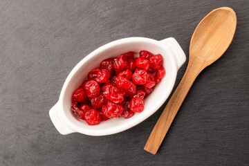 Dried sweet pitted cherries in white ceramic plate with wooden spoon on slate stone, macro, top view