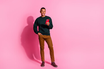 Fototapeta premium Full length photo of funky cool guy dressed pullover chatting modern device emtpy space isolated pink color background