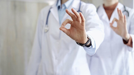 Two doctors is showing ok sign with fingers while standing in a hospital. Teamwork and success in medicine