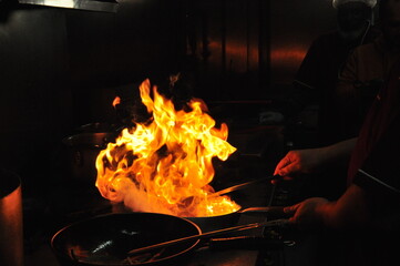 Chef cooking in the kitchen stove with flamed fire on a pan. Closeup hands cook food with fire