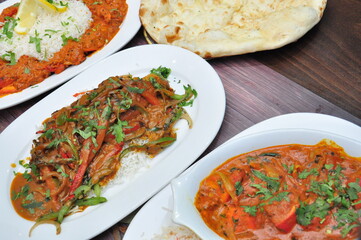 A top view of three plates of delicious Indian food on a table, chicken tikka masala with rice,  lamb korma, vegetable curry with naan bread
