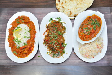 A top view of three plates of delicious Indian food on a table, chicken tikka masala with rice,  lamb korma, vegetable curry with naan bread
