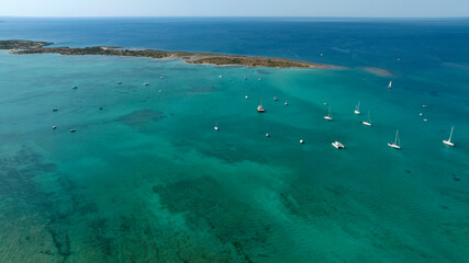 Obraz premium Aerial view of many boats anchored in the lagoon of Porto Cesareo, in Salento, Puglia, Italy. Here the water of the Mediterranean Sea has Caribbean colors. Boat holidays concept.