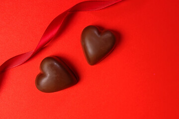 Fototapeta premium Delicious heart-shaped chocolates on a red background with a ribbon, Valentine's day celebration
