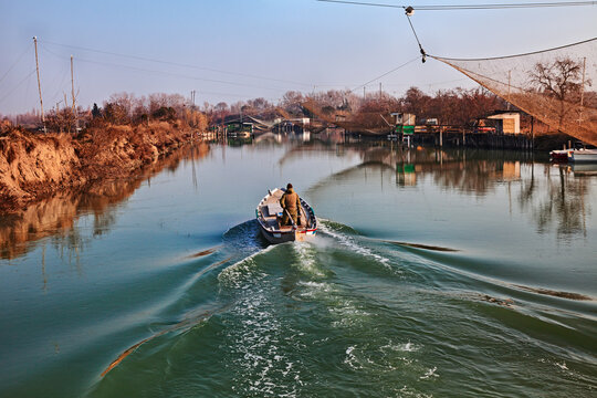 Ravenna, Emilia Romagna, Italy: landscape of the wetland in the nature reserve Po Delta Park, with fishing huts on the river and fisherman in the boat