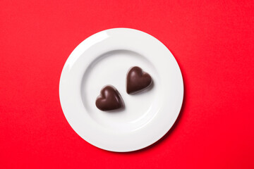 Delicious heart-shaped chocolates on a white plate on a red background for Valentine's day