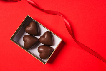 Heart shaped chocolate candies in a gift box on red background, top view. Valentine's day