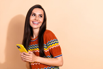 Portrait of pretty young lady hold phone look empty space wear t-shirt isolated on beige color background