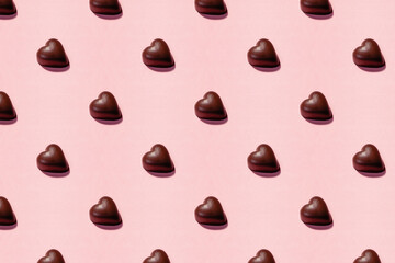 Heart-shaped chocolate pieces arranged on a pink background, romantic pattern