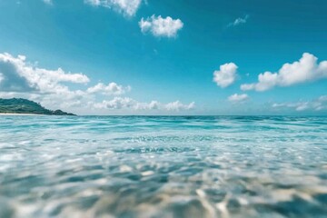 Obraz premium Close-up view of the crystal-clear turquoise ocean sea, with sunlight creating patterns on the water’s surface, reflecting the serenity and purity of tropical seas under a bright, cloud-filled sky.