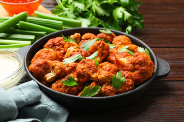 Tasty cauliflower buffalo wings, sauces and celery on wooden table, closeup