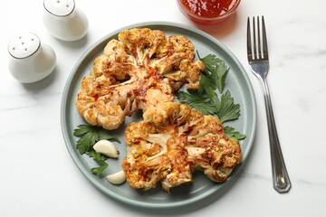 Delicious baked cauliflower steaks with garlic and parsley on white table, flat lay