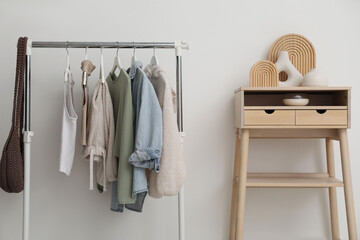 Rack with clothes and standing desk near white wall