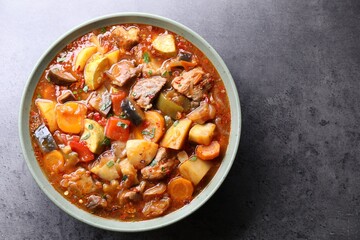 Delicious stew with vegetables in bowl on grey table, top view