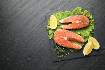 Fresh raw salmon steaks with spices, lemon, lettuce and rosemary on dark textured table, top view. Space for text